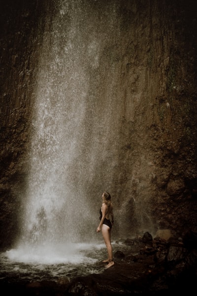白天，一名身穿黑色比基尼的女子坐在水瀑布附近的岩石上